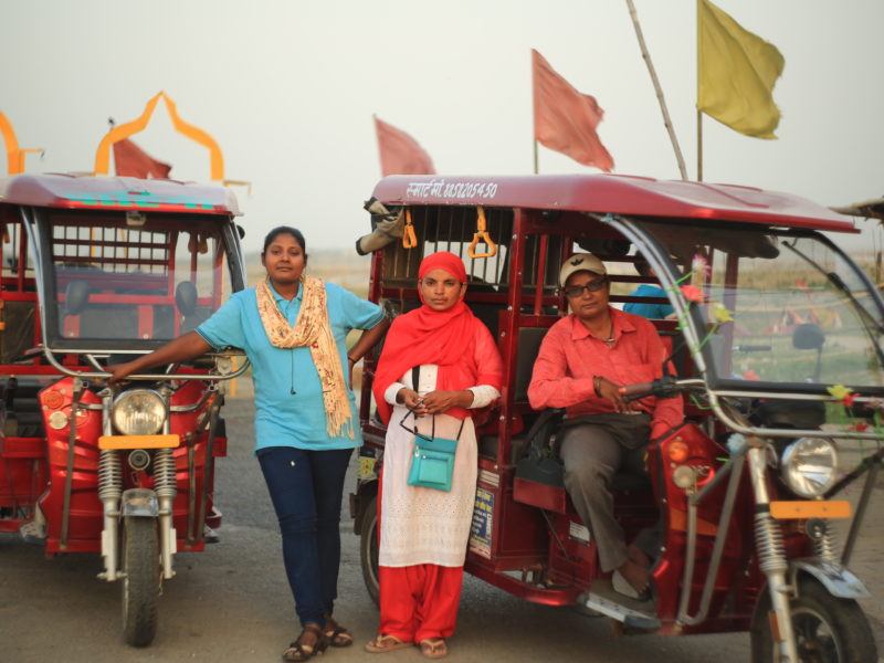 Three female e-rickshaw drivers in front of their rickshaws